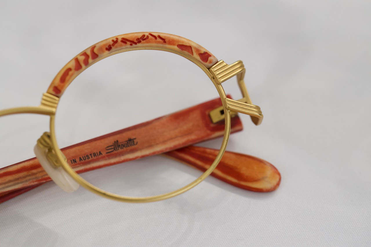 A pair of orange, vintage Silhouette eyeglasses with a gold frame.