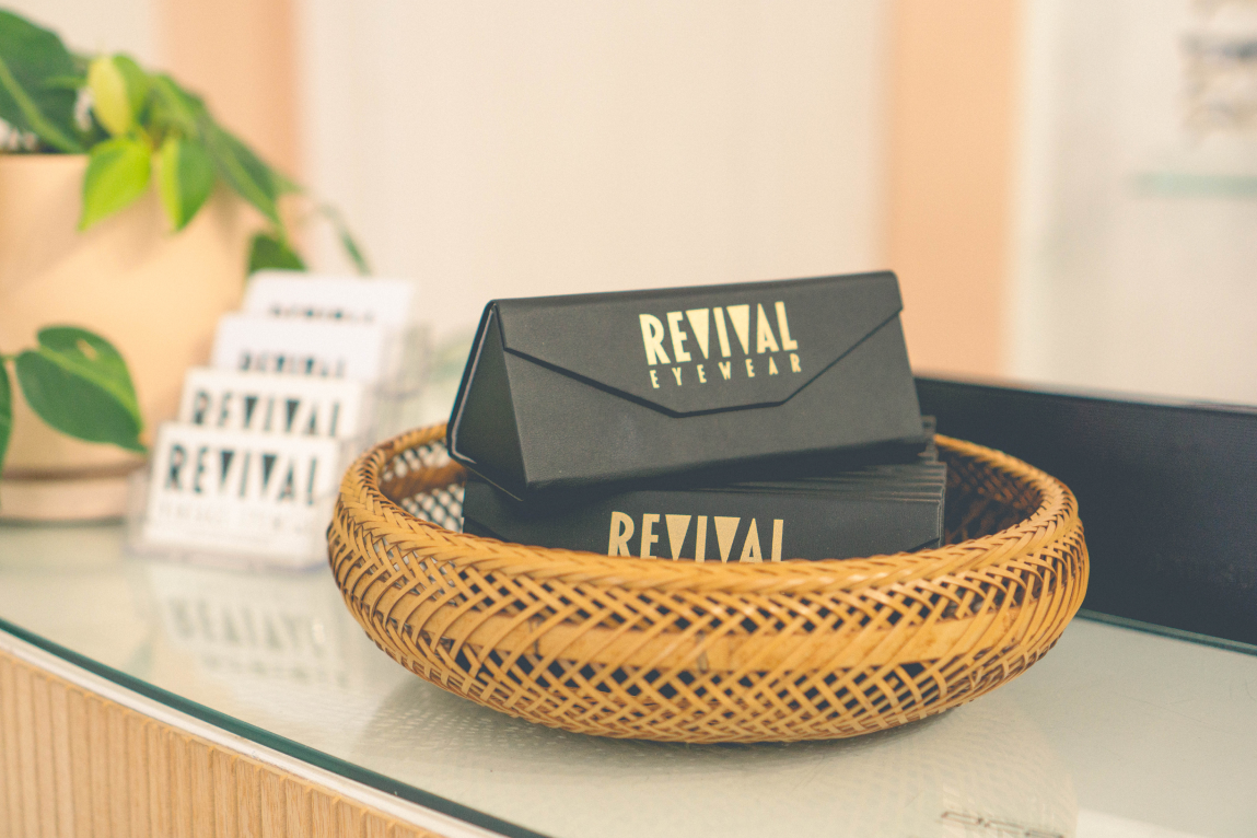 Sunglasses cases that say "Revival" in gold lettering sitting in a wicker basket on a counter. 
